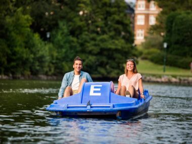 Happy friends pedal boating on river in city